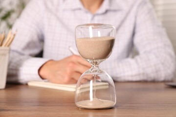 Deadline. Hourglass and man working at wooden table, selective focus
