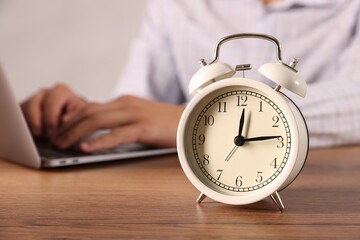 Deadline. Alarm clock and man working on laptop at wooden table, selective focus