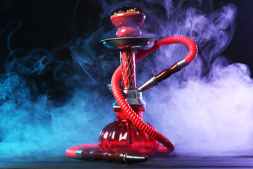 Hookah on wooden table with smoke in color lights against black background