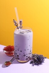 Tasty milk bubble tea in glass on white table against orange background
