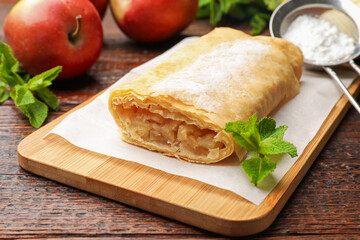 Tasty apple strudel with powdered sugar, mint and fruits on wooden table, closeup