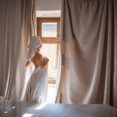 Young woman in a white towel standing by the window in the morning