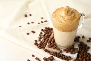 Delicious dalgona coffee in glass cup and beans on light table, closeup. Space for text