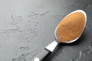 Spoon with instant coffee powder on dark textured table, closeup. Space for text