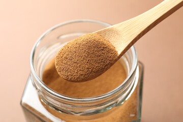 Spoon with instant coffee powder and jar on beige background, closeup