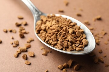 Spoon with granulated instant coffee on beige background, closeup