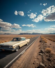 A vintage car drives along a long, empty road in a desert landscape. The sky is blue with fluffy clouds and distant mountains are visible.