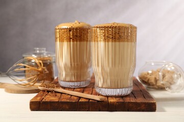 Delicious dalgona coffee in glasses, whisk, brown sugar and granules on light table, closeup