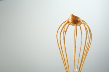 Making delicious dalgona coffee. Whisk with cream on light grey background, closeup. Space for text