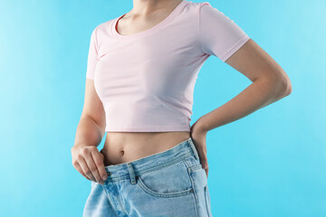 Woman wearing old jeans after weight loss on light blue background, closeup