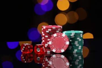 Casino chips and dice on mirror surface against blurred lights, closeup
