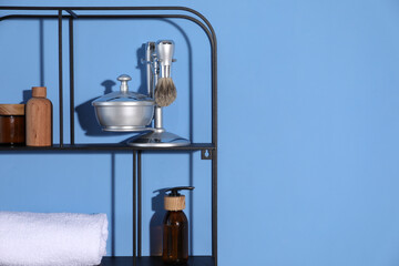 Metal shelving unit with towel and cosmetic products on blue background. Space for text
