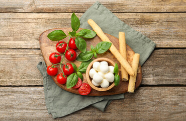 Tasty mozzarella cheese balls, tomatoes, basil and grissini on wooden table, top view