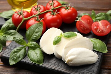Tasty mozzarella cheese, tomatoes and basil on wooden table, closeup