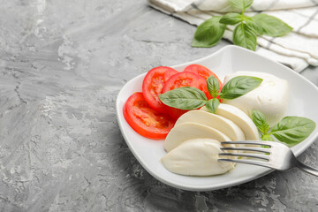 Tasty mozzarella cheese, tomato and basil on grey table, closeup. Space for text