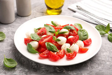 Tasty salad Caprese with mozzarella, tomatoes, basil and spices on grey table, closeup