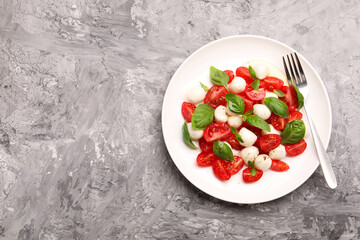 Tasty salad Caprese with mozzarella, tomatoes, basil and spices on grey table, top view. Space for...