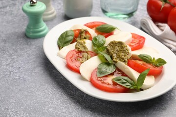 Tasty salad Caprese served with pesto sauce on grey table, closeup. Space for text