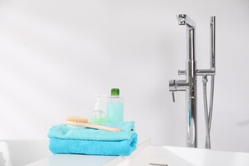 White board with soft towels, brush and cosmetic products on tub indoors
