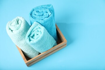 Different soft towels in wooden basket on light blue background, above view. Space for text