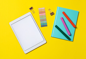 Tablet and different stationery on yellow background, flat lay