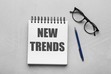 New Trends inscription in notebook, glasses and pen on red background, top view