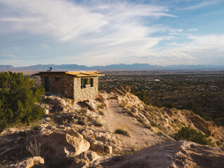 Fototapeta premium Small Stone and Wood Cabin on a Hilltop Overlooking a Vast Desert Landscape