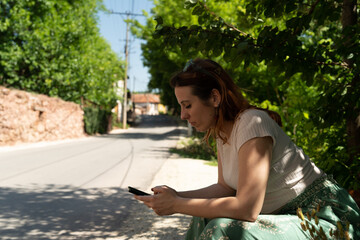 Woman typing messages on a mobile phone by the road