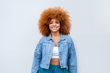 Young stylish latina woman student or model in denim jacket standing isolated on background looking at camera. Beautiful curly afro hair african american girl in trendy clothes smile with copy space