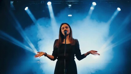 Silhouette of female singer standing under spotlight holding microphone on stage - Powered by Adobe