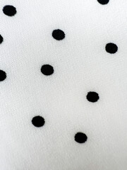 A detailed close-up of soft white satin fabric with classic black polka dots. Elegant, retro-style...