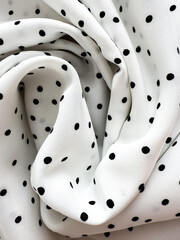 A detailed close-up of soft white satin fabric with classic black polka dots. Elegant, retro-style...
