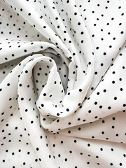 A detailed close-up of soft white satin fabric with classic black polka dots. Elegant, retro-style textile background for fashion or design use