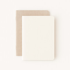 Fototapeta premium Top-down view of two minimalist notebooks stacked on a white background. One ivory matte, one linen-textured beige. Clean, neutral, unbranded design. Ideal for back-to-school or lifestyle themes. 