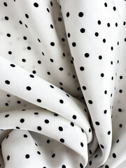 A detailed close-up of soft white satin fabric with classic black polka dots. Elegant, retro-style...