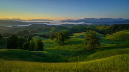 Fototapeta premium Summer sunset over a mountain landscape with a verdant valley and rolling hills under a vibrant sky