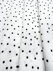 A detailed close-up of soft white satin fabric with classic black polka dots. Elegant, retro-style...