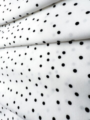 A detailed close-up of soft white satin fabric with classic black polka dots. Elegant, retro-style...