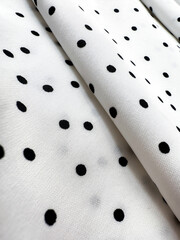A detailed close-up of soft white satin fabric with classic black polka dots. Elegant, retro-style...