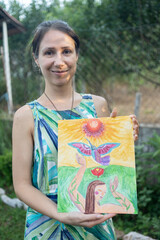 Creative female painting student in a summer painting school, proudly showing off her finished painting, an outdoor smiling portrait