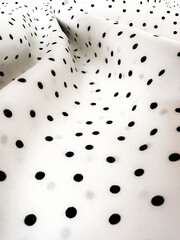 A detailed close-up of soft white satin fabric with classic black polka dots. Elegant, retro-style textile background for fashion or design use