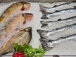 A market display of fresh whole fish arranged on a crushed ice, featuring silver and golden scaled...