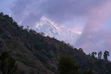 A breathtaking view of the snow-capped peak of Annapurna South when the clouds softly hug the mountains in great Himalayas in Nepal.