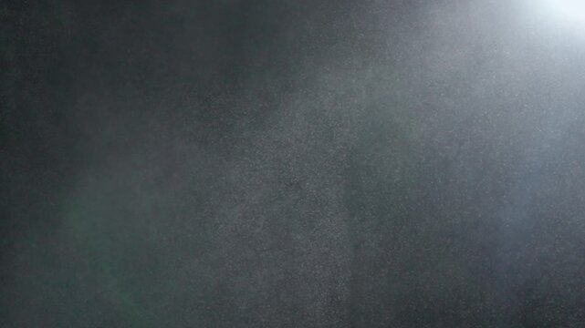 Many dust particles white powder floating on empty black contrast background in spotlight. Slow motion.