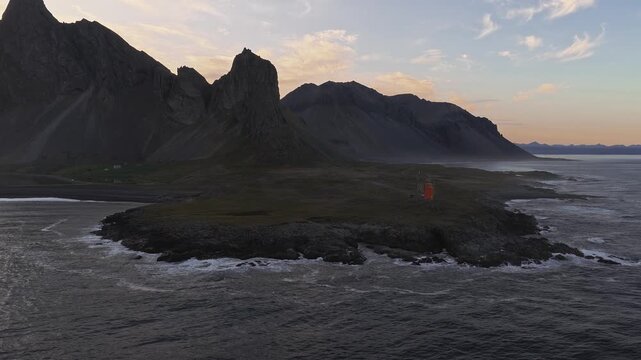 Aerial view of Stokksnes peninsula in Iceland with Vestrahorn mountain, rugged cliffs, Hvalnes Lighthouse, and panning motion revealing the coastline.