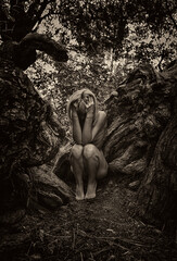 Woman in fetal position among tree roots  symbolizing connection with nature and rebirth.