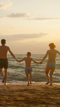 A cheerful family sprints along the sandy shore eager to dive into the ocean's embrace as the sun sets casting a golden glow.
