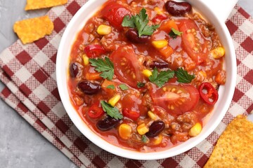 Tasty chili con carne in bowl and nachos on grey textured table, flat lay