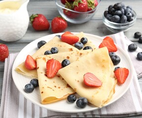 Delicious crepes with berries and cream on grey wooden table, closeup