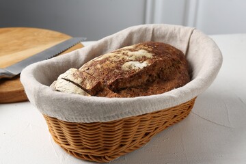 Fresh rye bread in wicker basket on white textured table against light grey wall, closeup